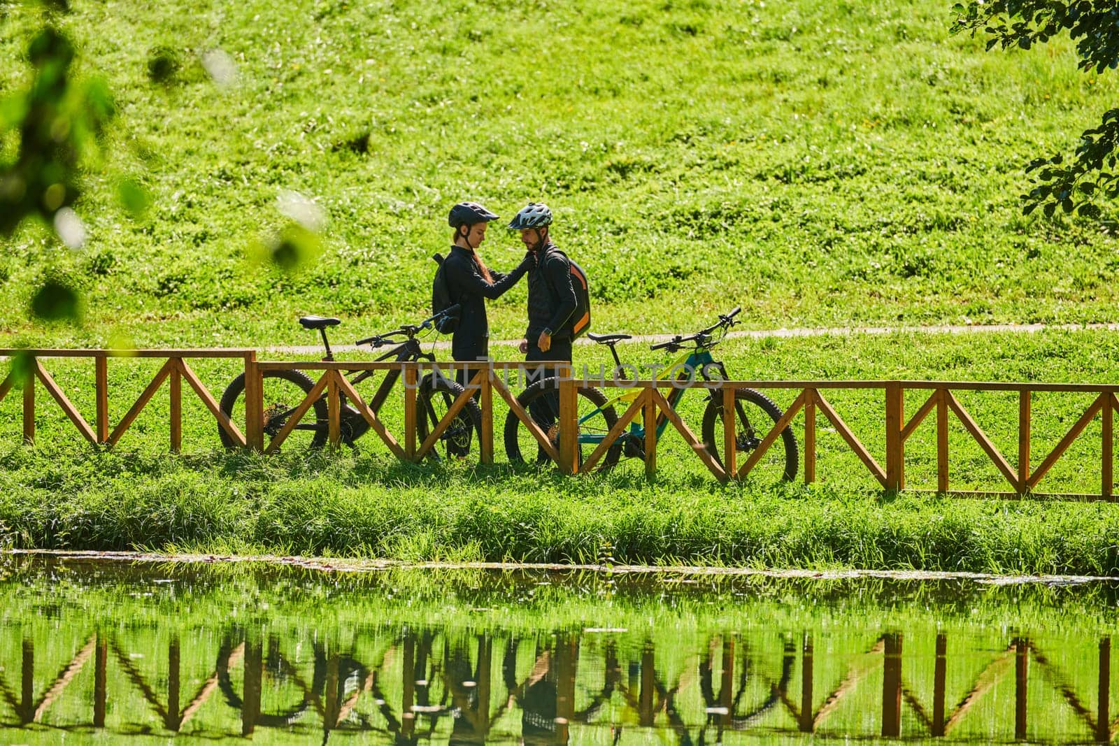 A blissful couple, adorned in professional cycling gear, enjoys a romantic bicycle ride through a park, surrounded by modern natural attractions, radiating love and happiness.