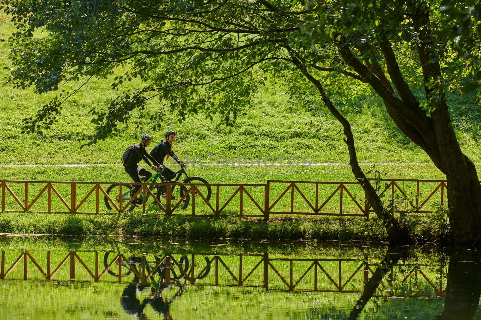 A blissful couple, adorned in professional cycling gear, enjoys a romantic bicycle ride through a park, surrounded by modern natural attractions, radiating love and happiness.