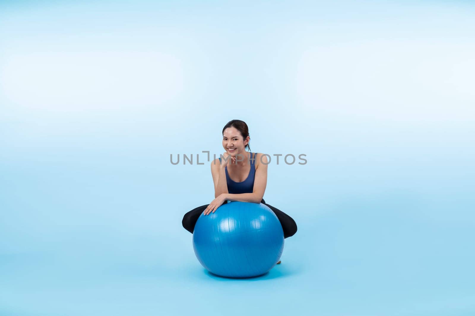 Young attractive asian woman portrait in sportswear with fit ball targeting on abs muscle for effective energetic daily workout routine. Studio shot and isolated background. Vigorous