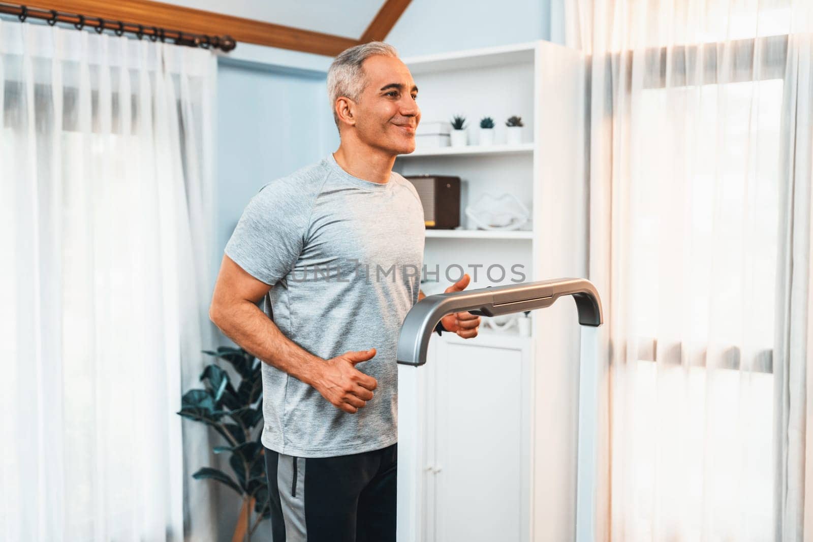 Active senior man running on tread running machine at home together as fitness healthy lifestyle and body care after retirement for pensioner. Clout