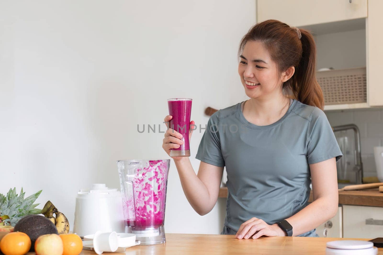 Young attractive Asian woman makes a fruit smoothie in the kitchen. Take care of your health by eating fruits and vegetables to add vitamins..