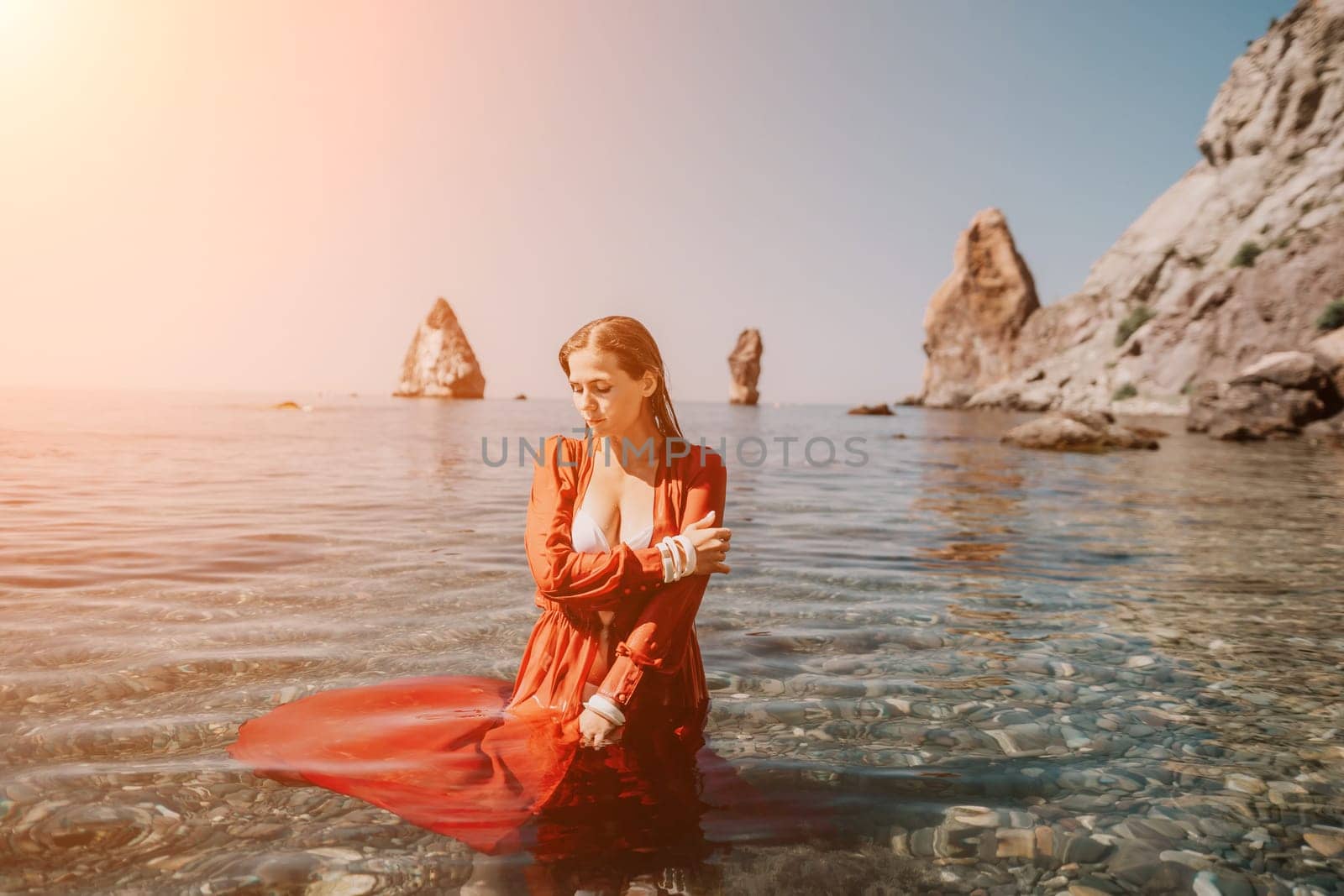Woman travel sea. Happy tourist in red dress enjoy taking picture outdoors for memories. Woman traveler posing in sea beach, surrounded by volcanic mountains, sharing travel adventure journey by panophotograph