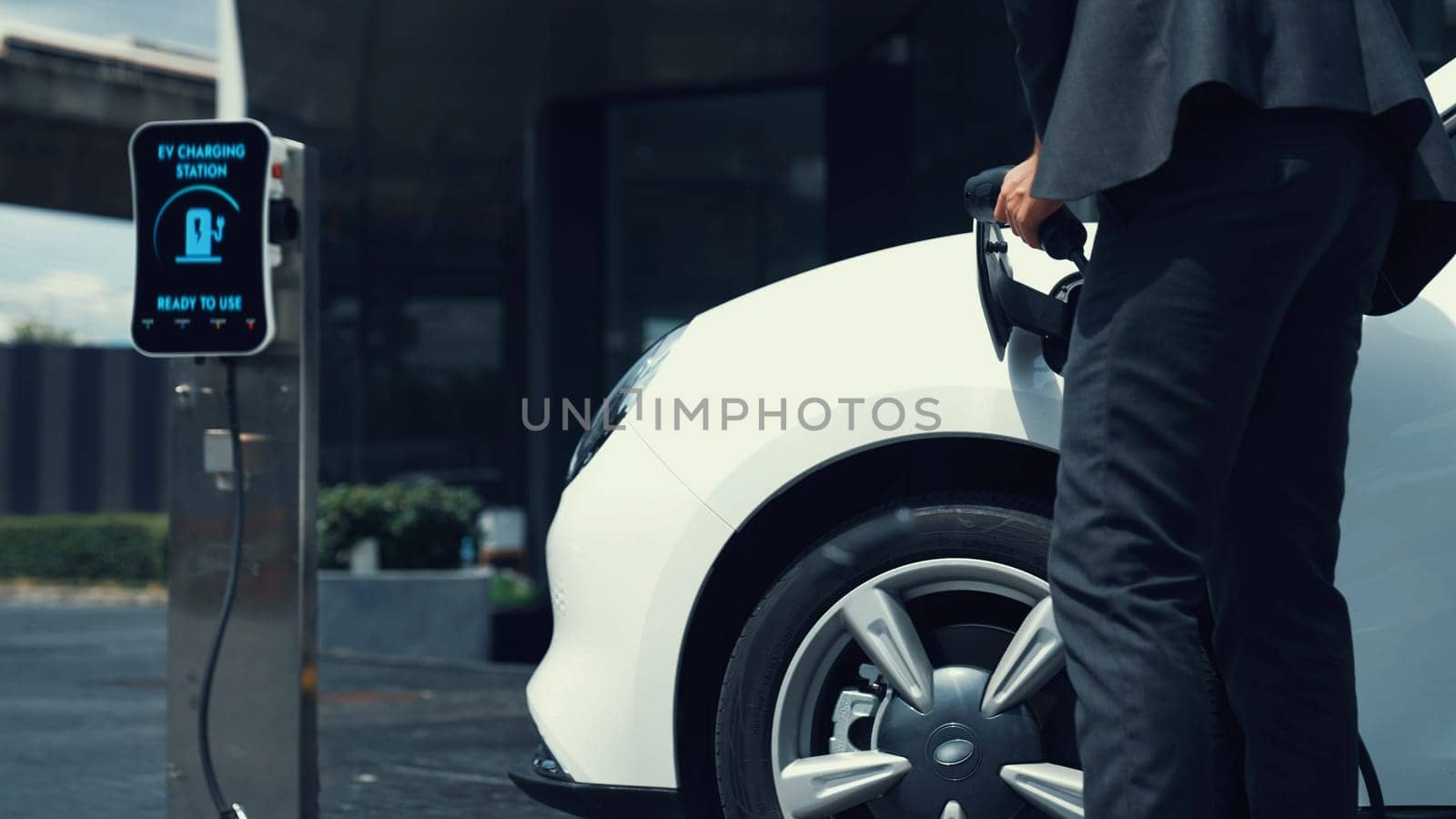 Businessman recharge his electric car from charging station at city center or public car park. Eco friendly rechargeable car using alternative clean energy in urban city lifestyle.Peruse