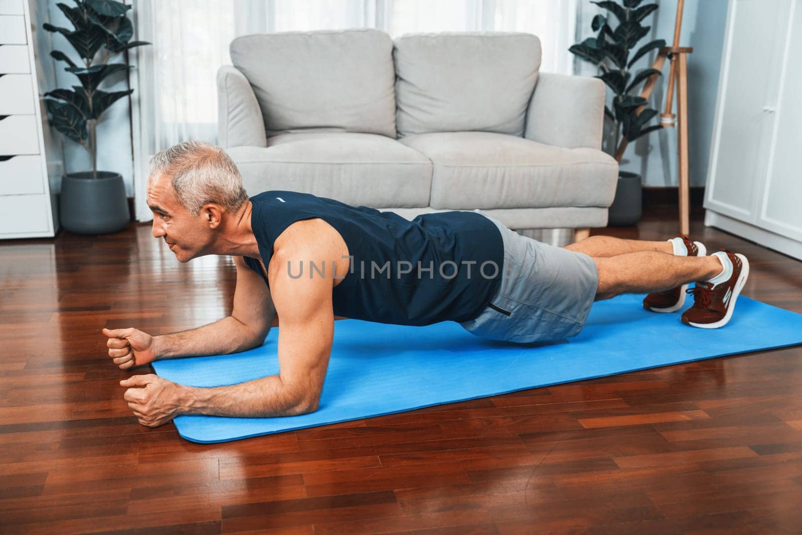 Athletic and sporty senior man planking on fitness exercising mat at home exercise as concept of healthy fit body lifestyle after retirement. Clout