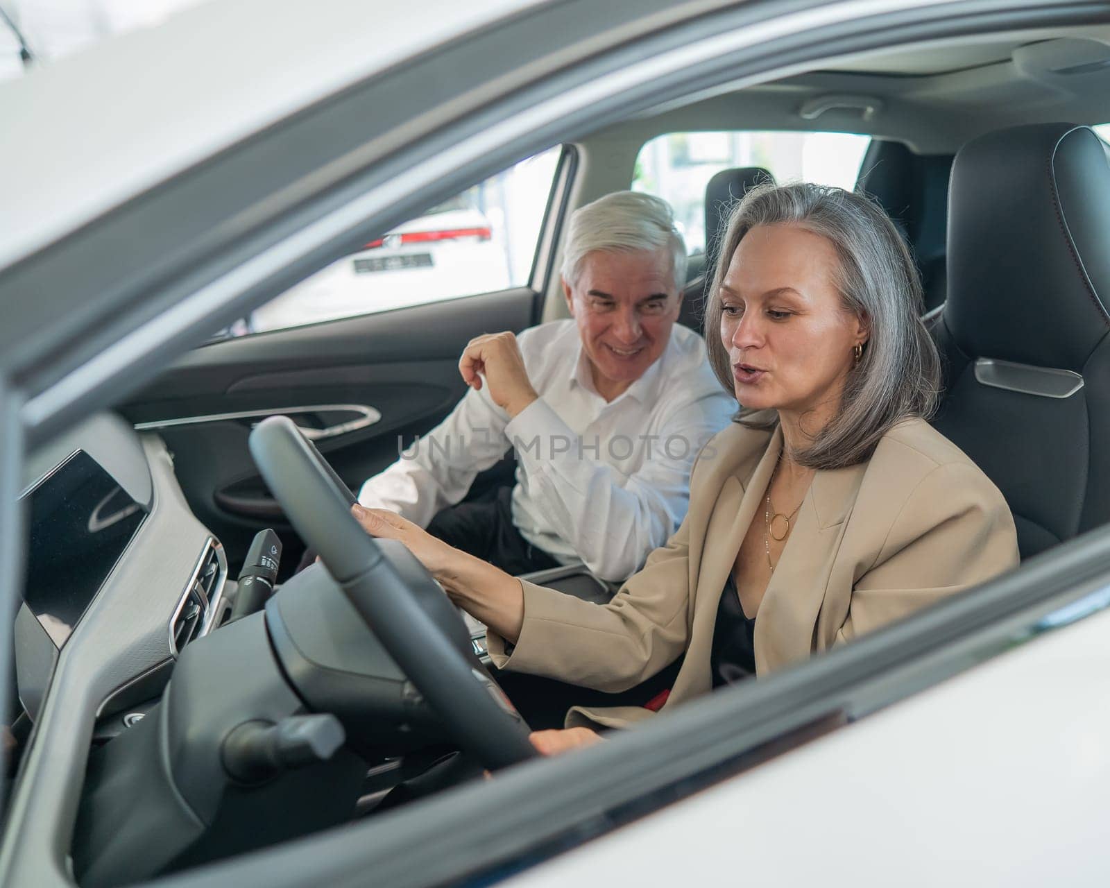 An elderly couple chooses a new car at a car dealership. Mature woman driving. by mrwed54