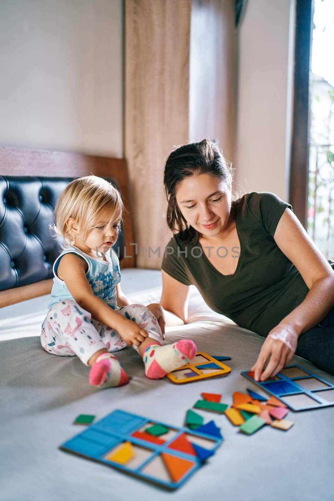Little girl looks at her mother putting together a puzzle on the bed. High quality photo