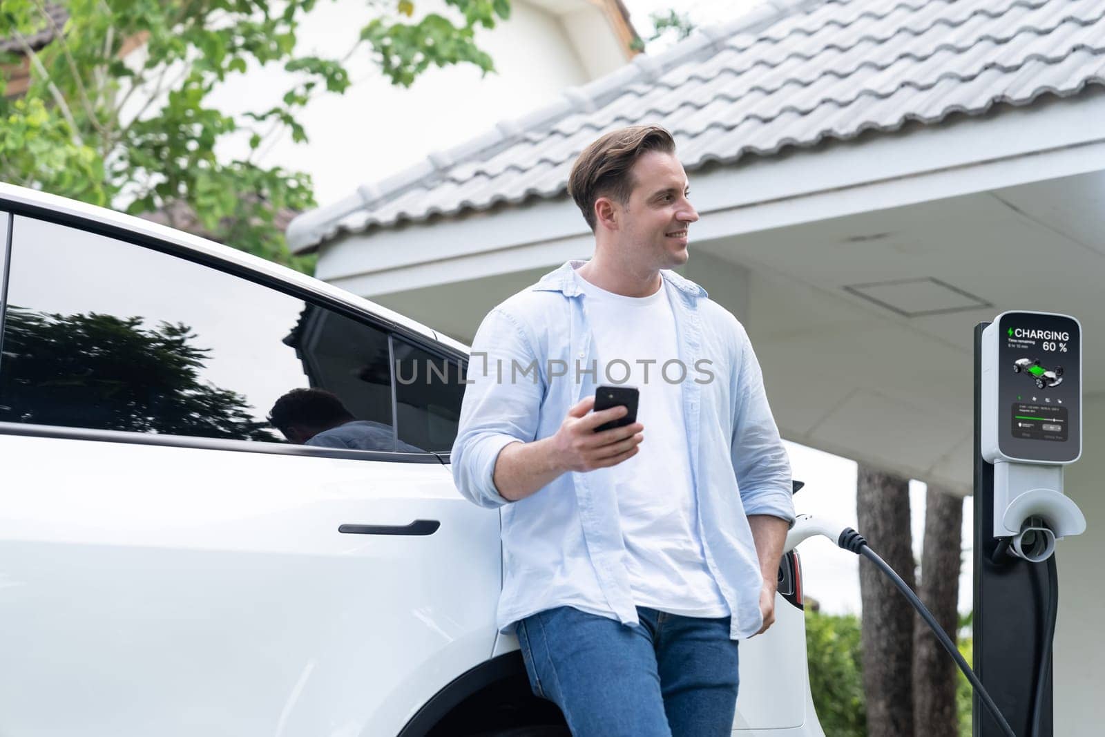 Modern eco-friendly man recharging electric vehicle from home EV charging station. Innovative EV technology utilization for tracking energy usage to optimize battery charging at home. Synchronos