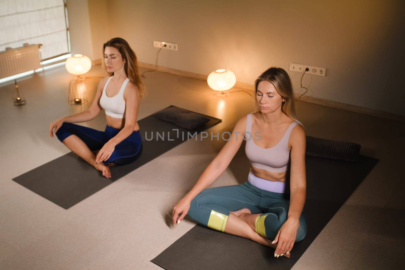 a couple of women performing breathing exercises while sitting on a yoga mat. yoga meditation in the fitness room.