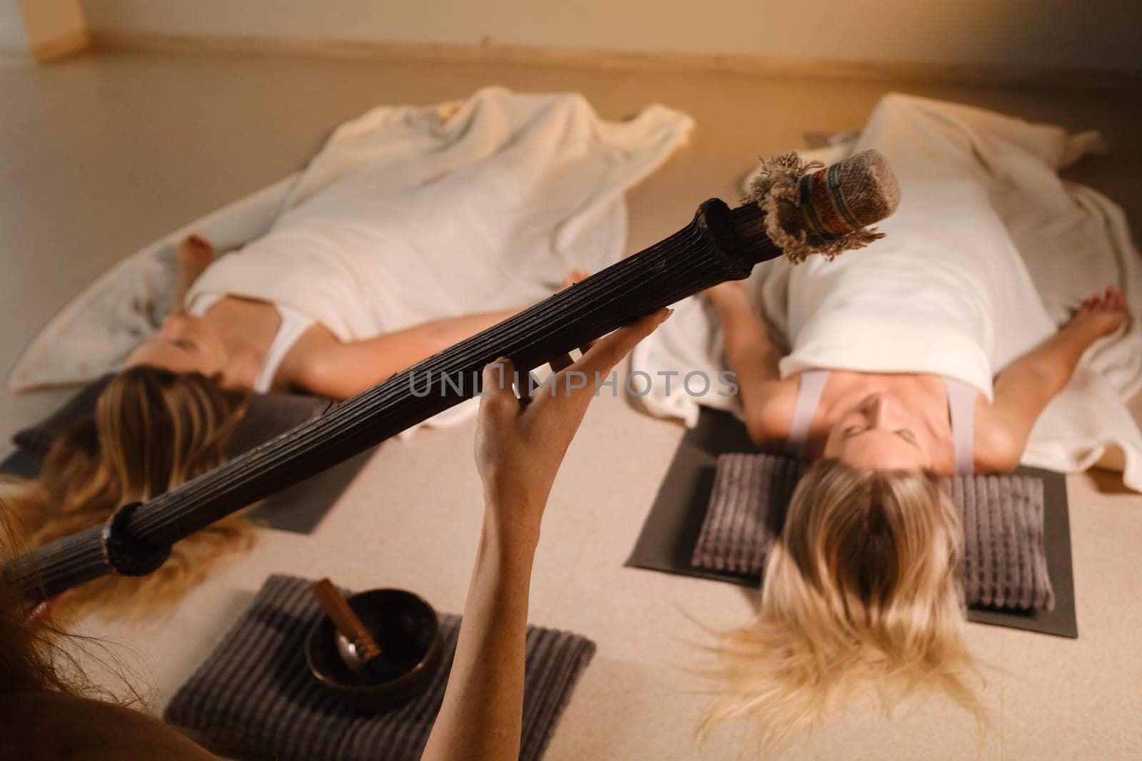 girls, lying on the floor, relax under the sound instrument of the rain staff in the fitness room.