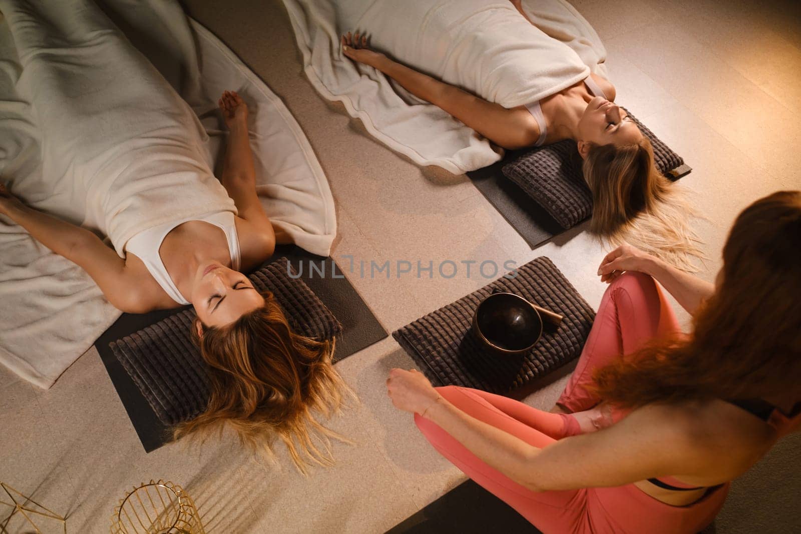 girls lying on the floor relax to the sounds of a Tibetan bowl in the fitness room by Lobachad