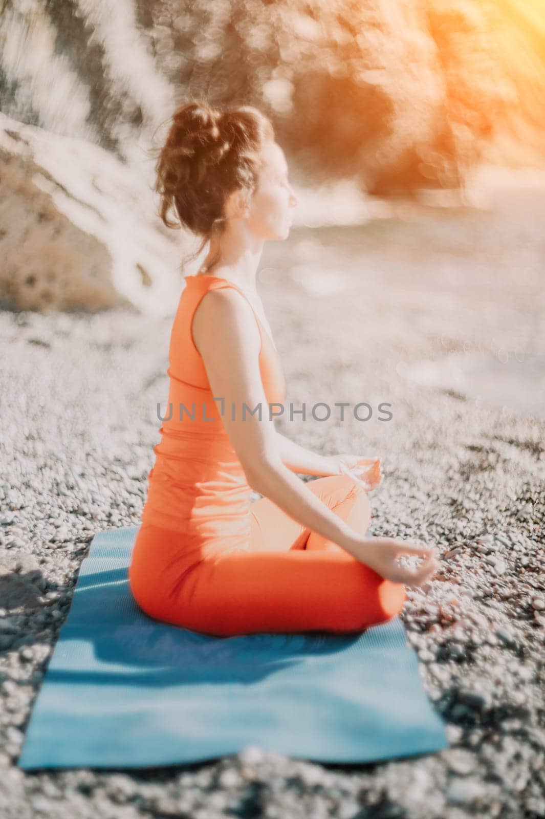 The woman in a red suit practicing yoga on stone at sunrise near the sea. Young beautiful girl in a red bathing suit sits on the seashore in lotus position. Yoga. Healthy lifestyle. Meditation