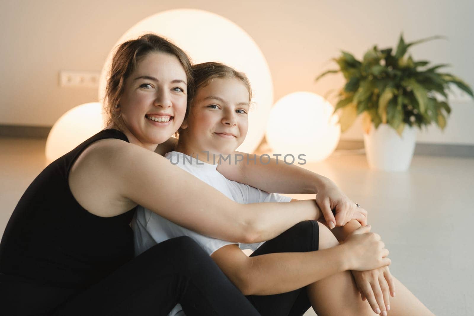 portrait of a mother and daughter of a teenager in sports clothes hugging, who are together in a fitness room. the concept of family sports by Lobachad