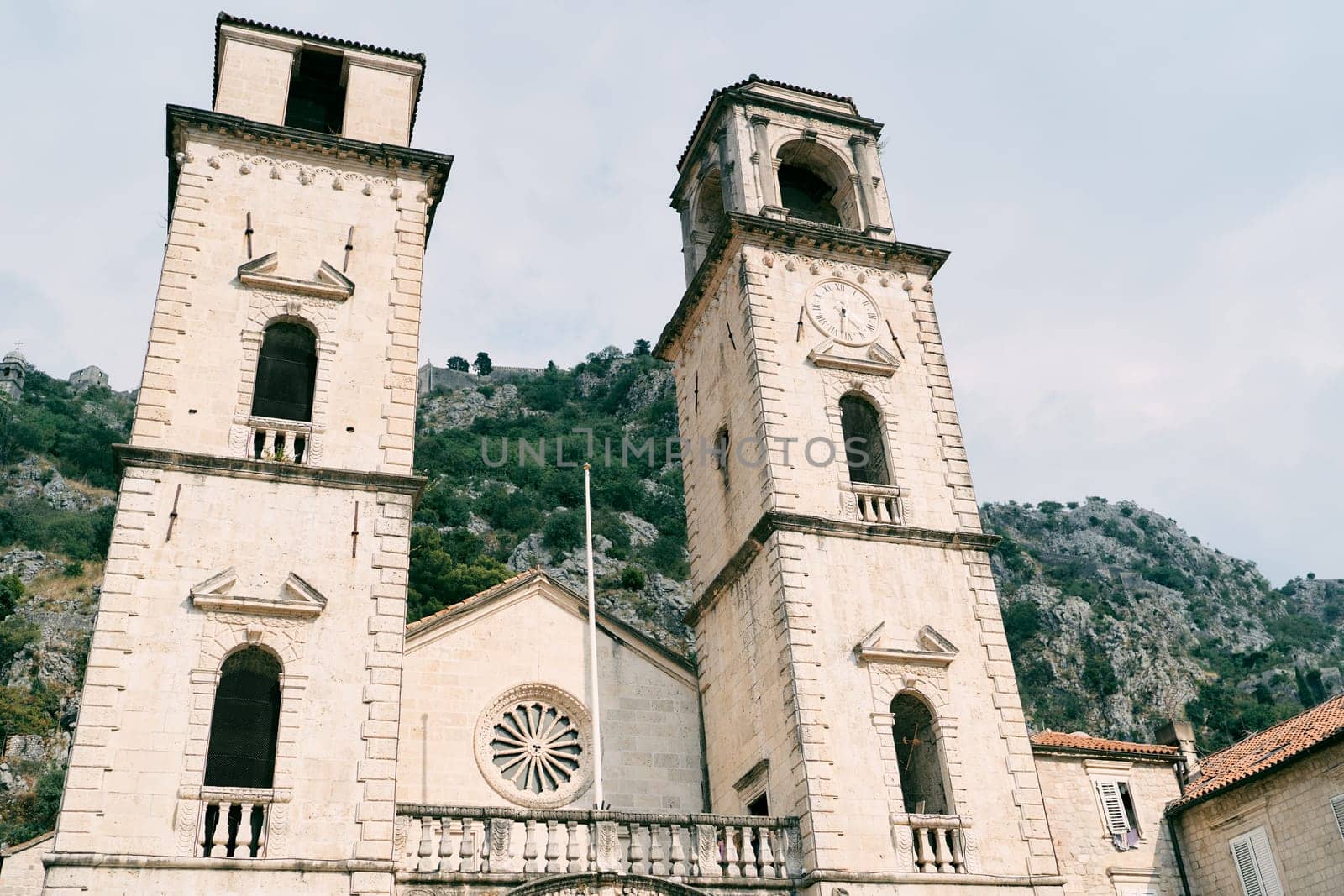 Bell towers of the Cathedral of St. Tryphon against the backdrop of green mountains. Kotor, Montenegro by Nadtochiy