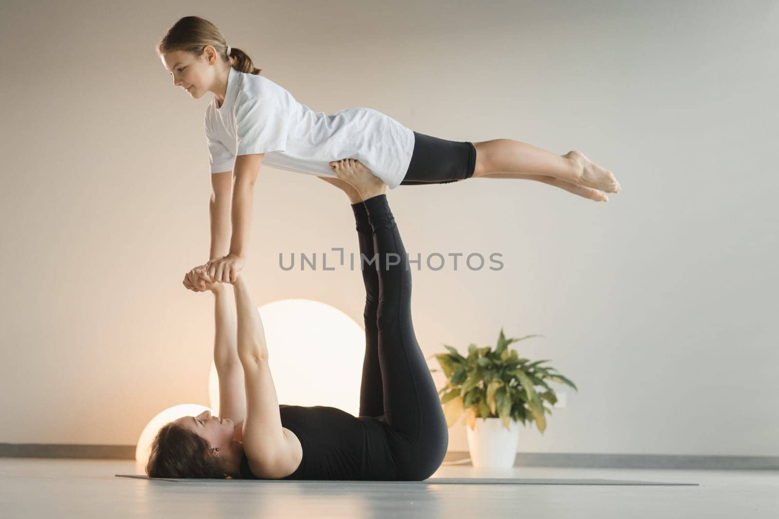 Mom and teenage daughter do gymnastics together in the fitness room. A woman and a girl train in the gym.