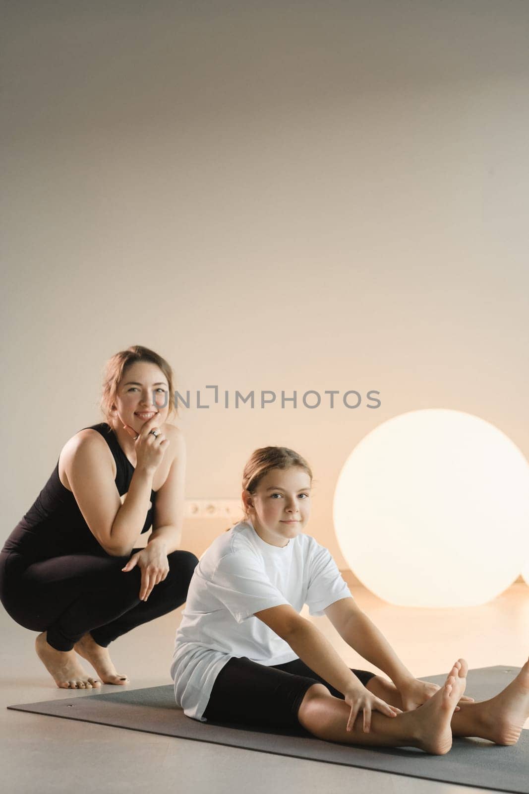 Mom and teenage daughter do gymnastics together in the fitness room. A woman and a girl train in the gym.