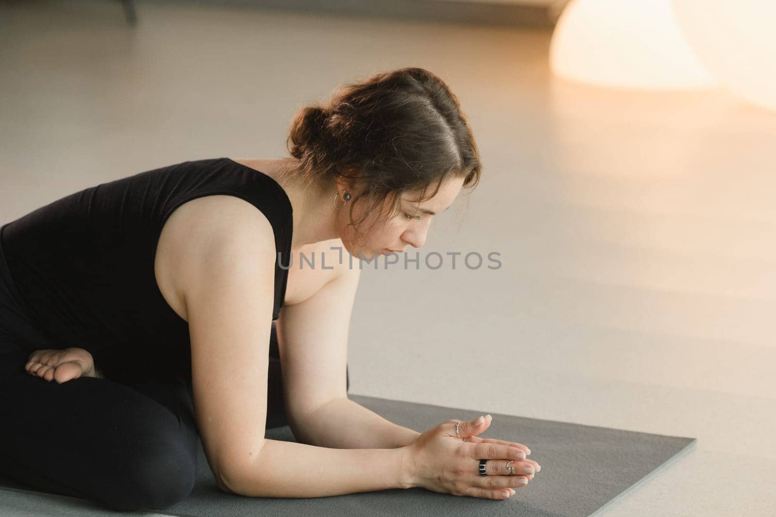 A girl in black sportswear does yoga on a mat in the fitness room.