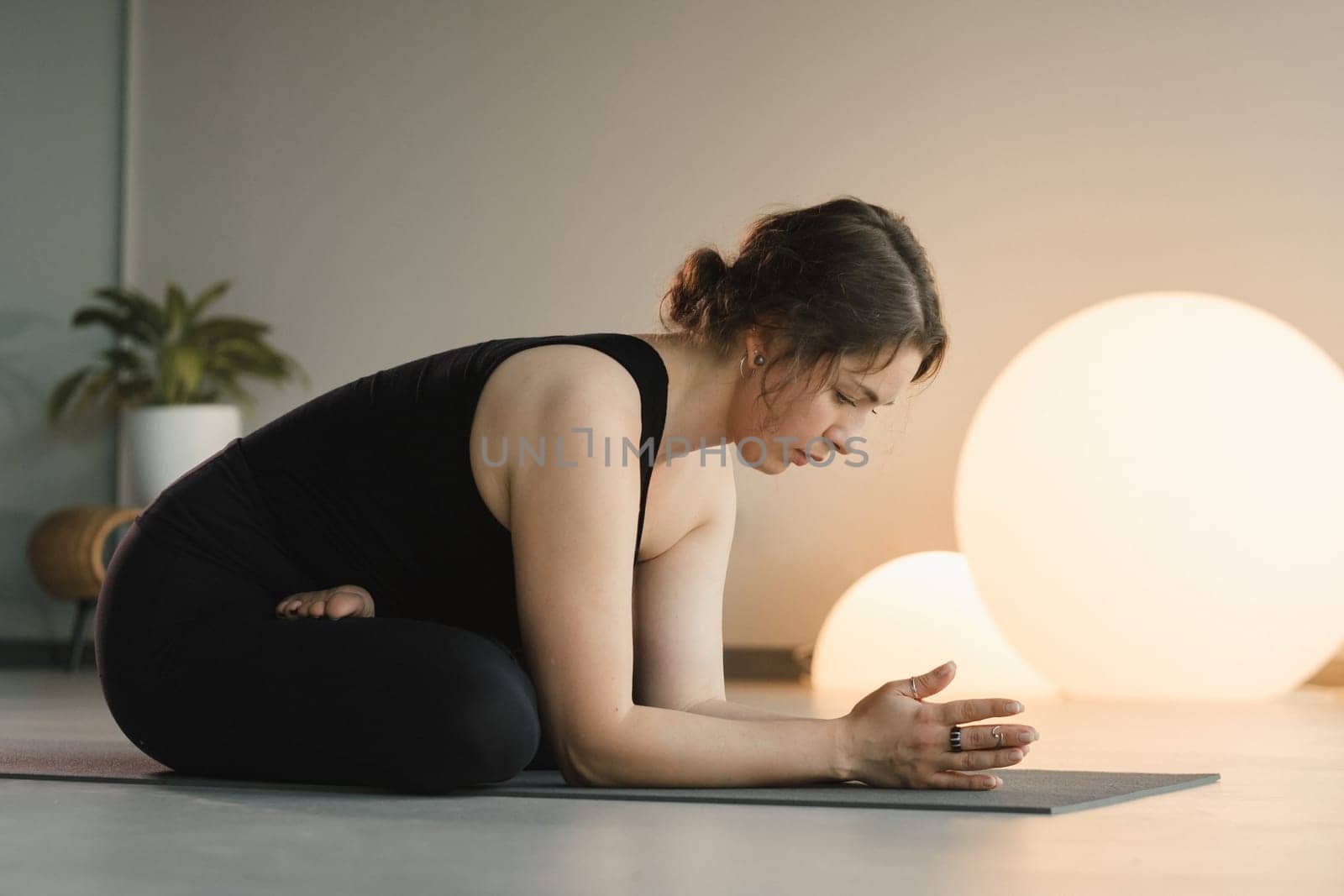 A girl in black sportswear does yoga on a mat in the fitness room by Lobachad