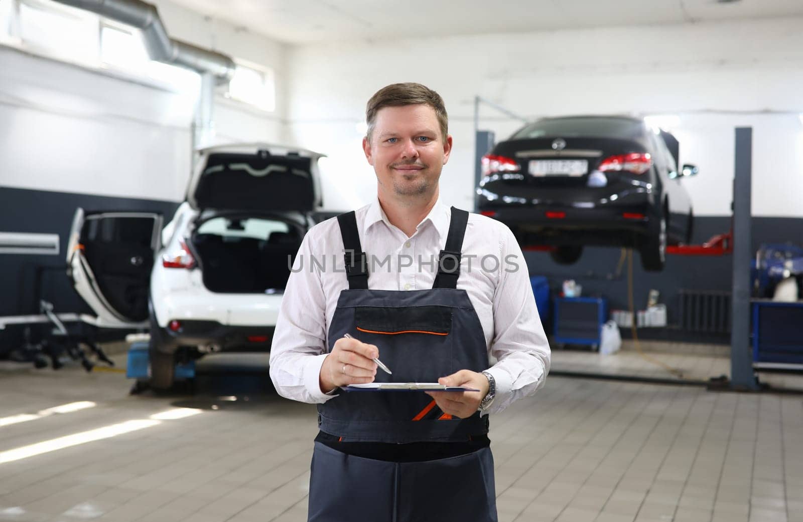 Young professional auto mechanic holding clipboard with pen. Auto insurance and car service concept