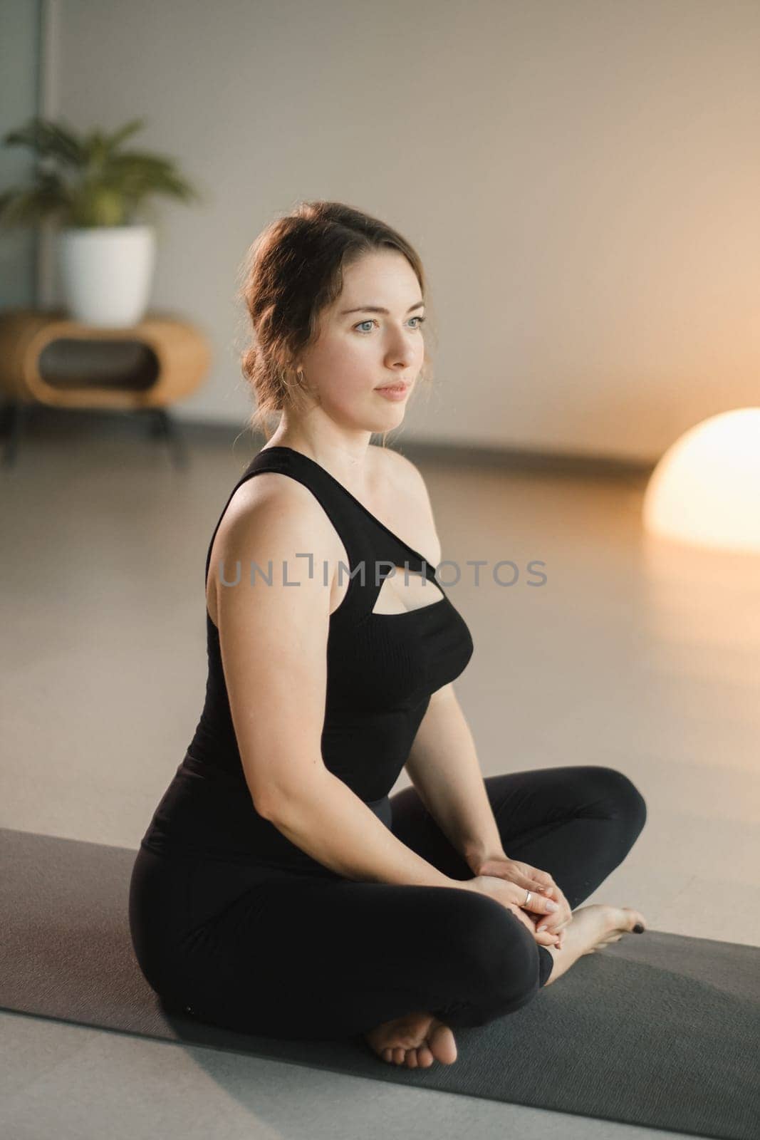 A girl in black sportswear does yoga on a mat in the fitness room by Lobachad