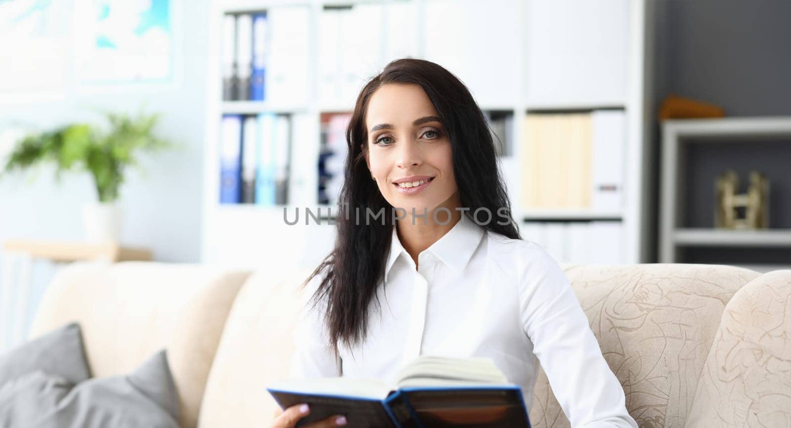 Beautiful smiling woman is reading book in living room. Education and reading books concept