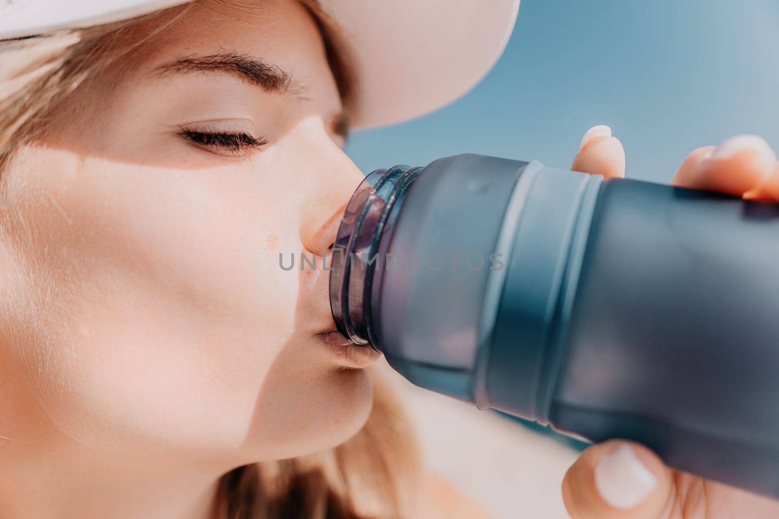 Fintess woman drinking water. Happy, active middle aged woman standing on beach and drinking water after excersise. Concept of lifestyle, sport. Close up.