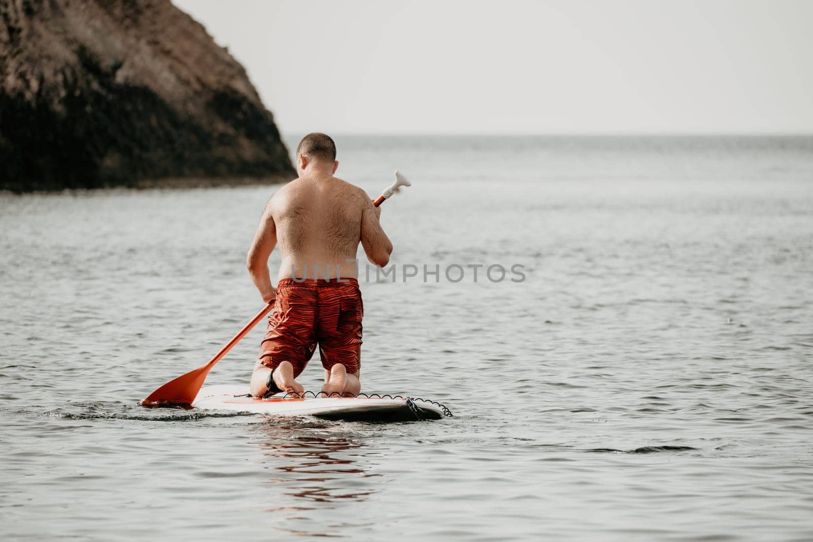 Active mature male paddler with his paddleboard and paddle on a sea at summer. Happy senior man stands with a SUP board. Stand up paddle boarding - outdor active recreation in nature. by panophotograph