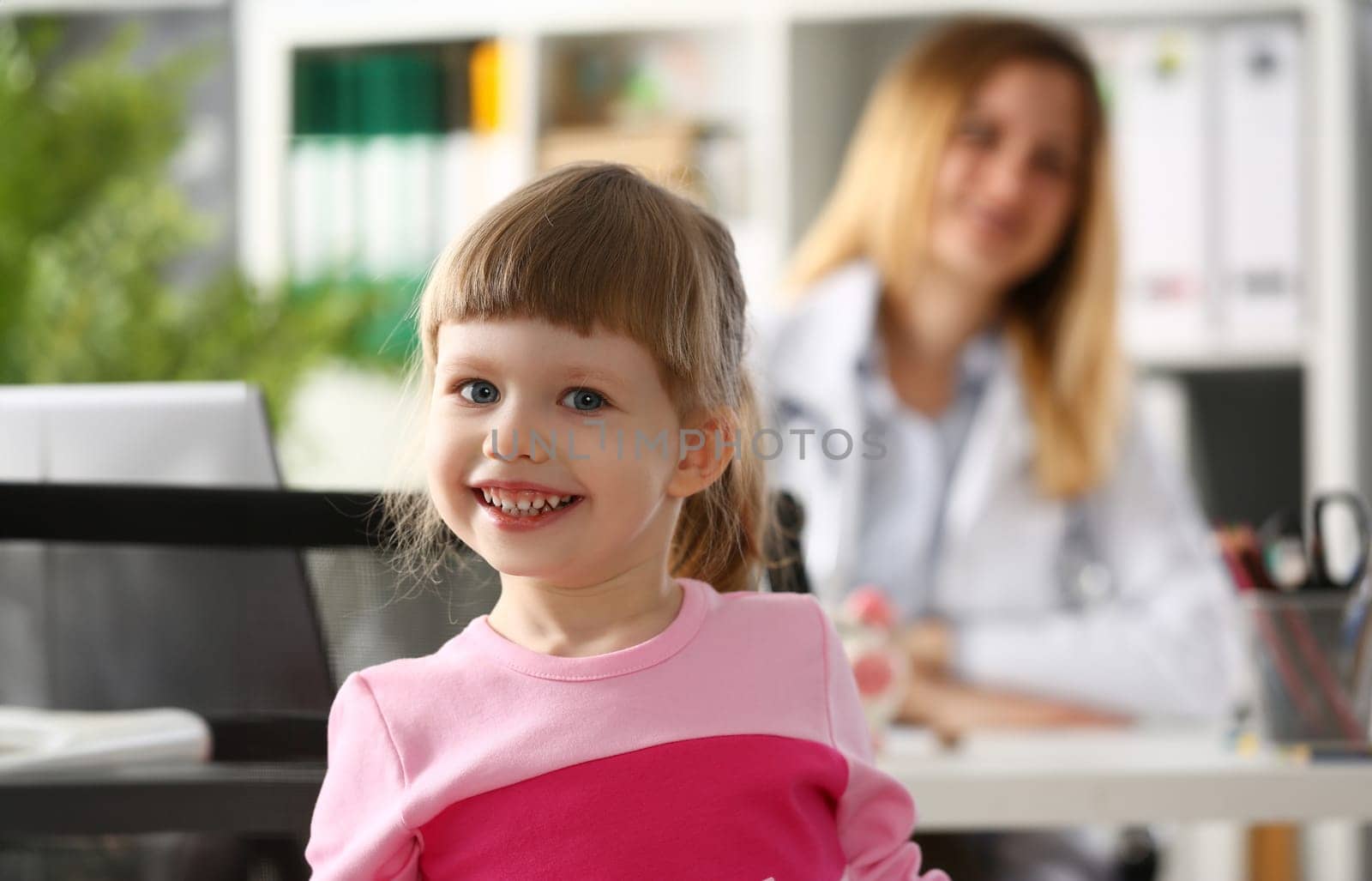 Portrait of little smiling baby girl in background sits doctor. Children health insurance and pediatrician services