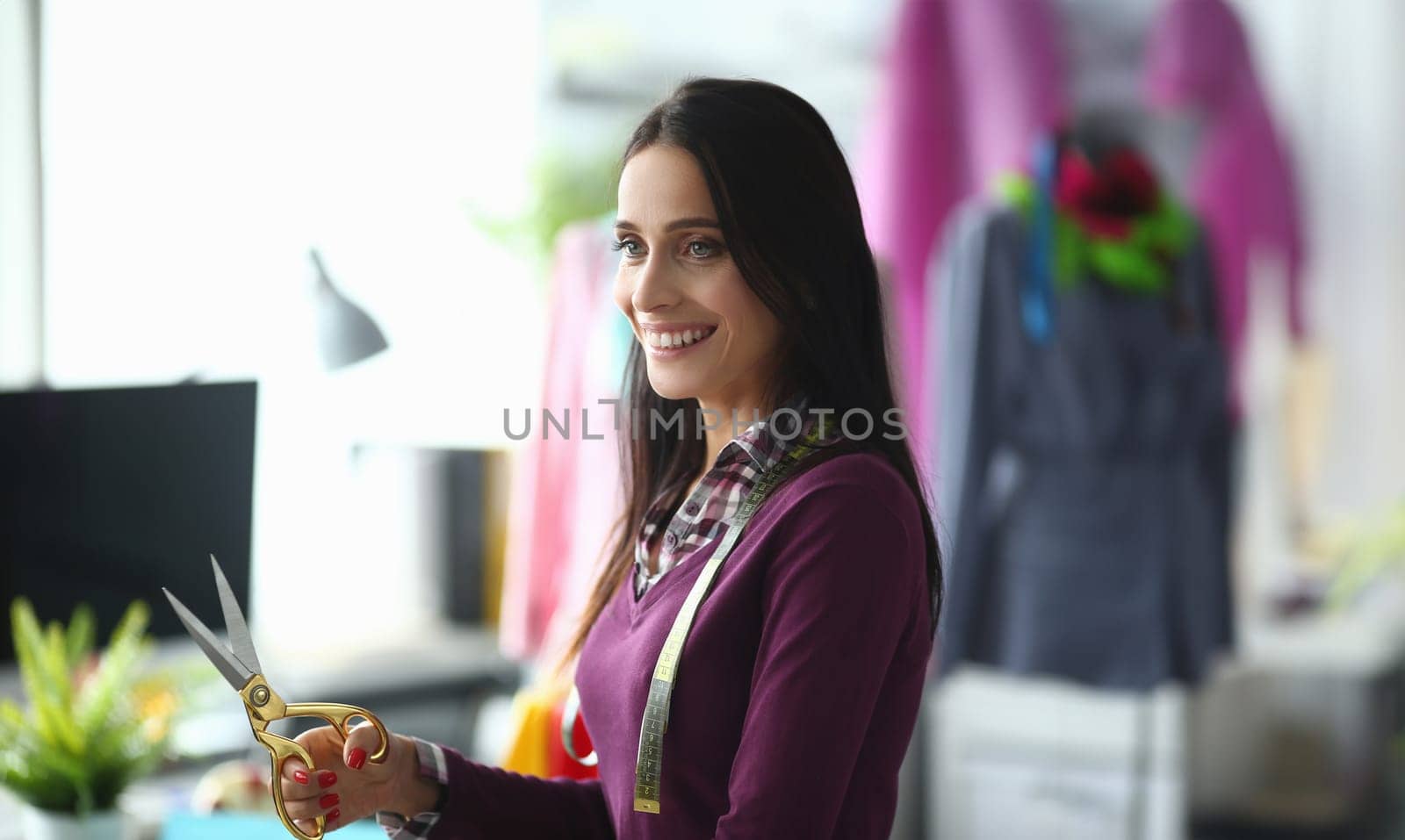 Smiling female fashion designer with scissors in hands in atelier. Tailoring service concept