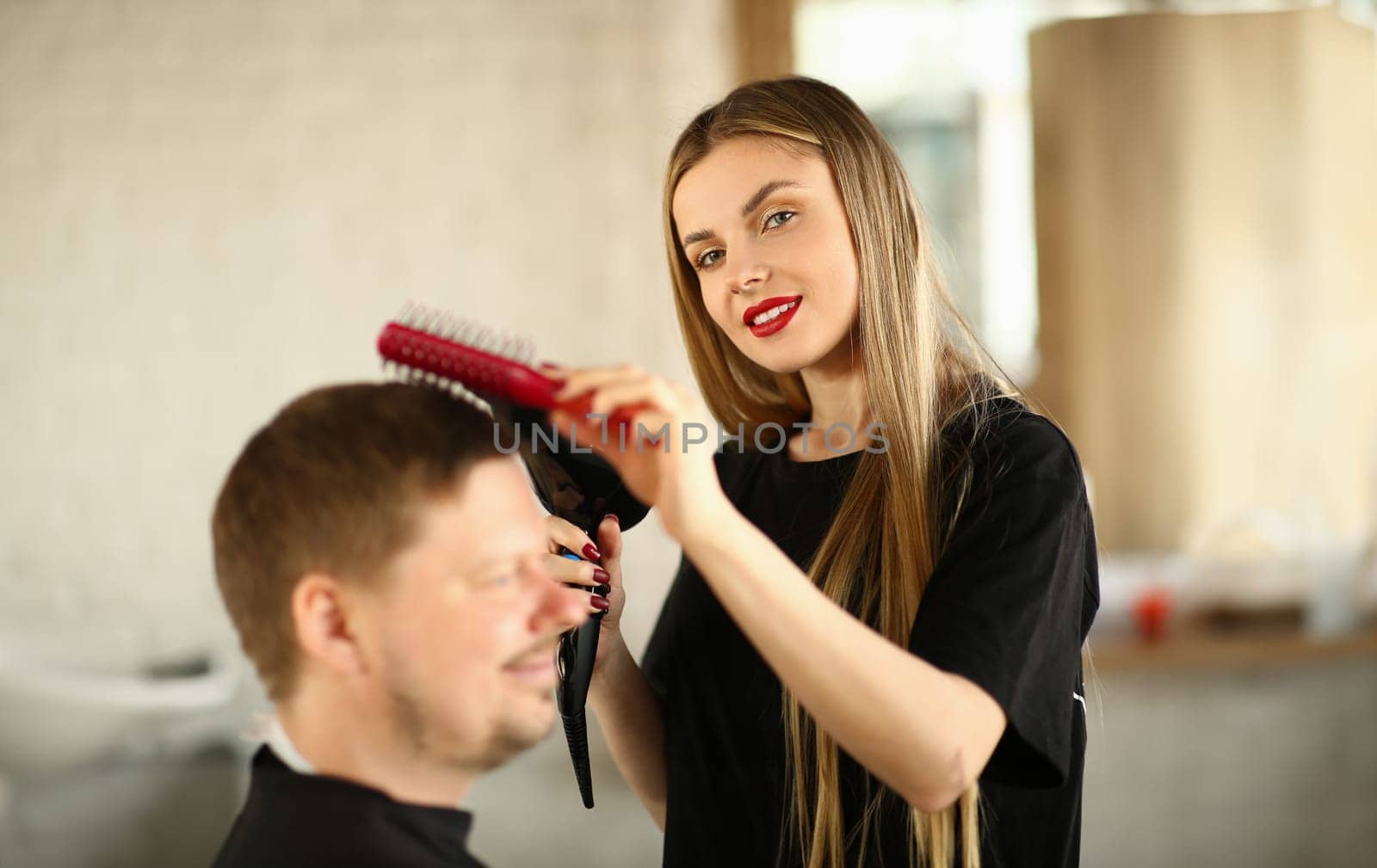 Woman in hairdresser hairdresser makes ahairstyle with hair dryer for male client. Stylish trendy hairstyle concept