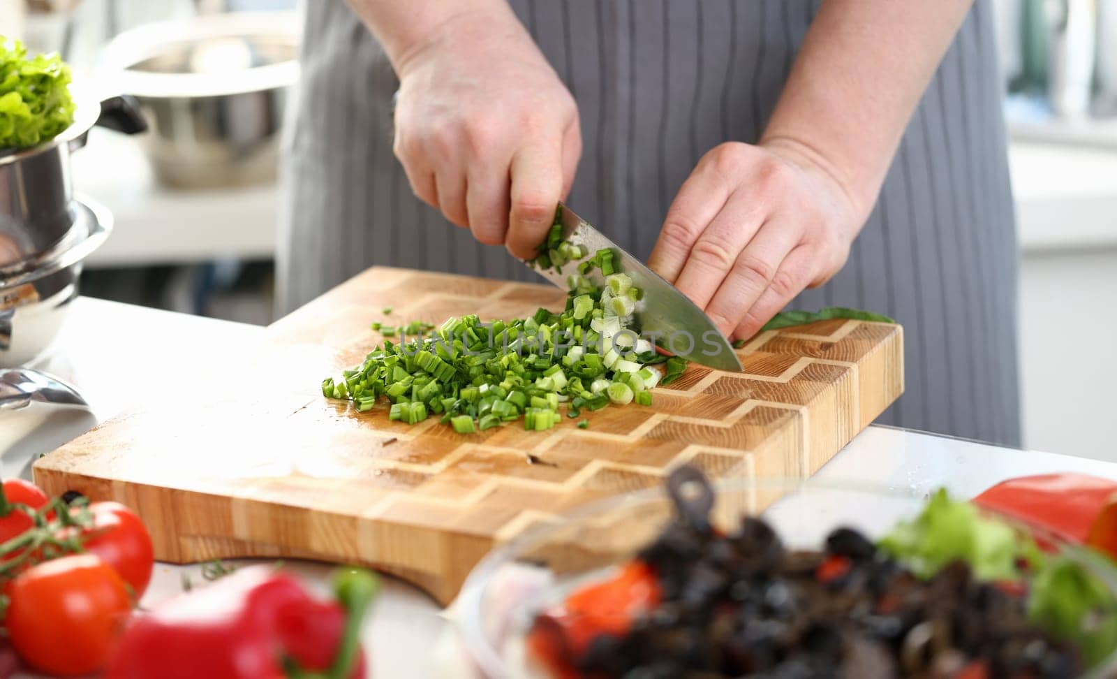 Closeup of hands of cook holding knife for cutting green onions. Sliced fresh green onions and cooking vegetables in kitchen