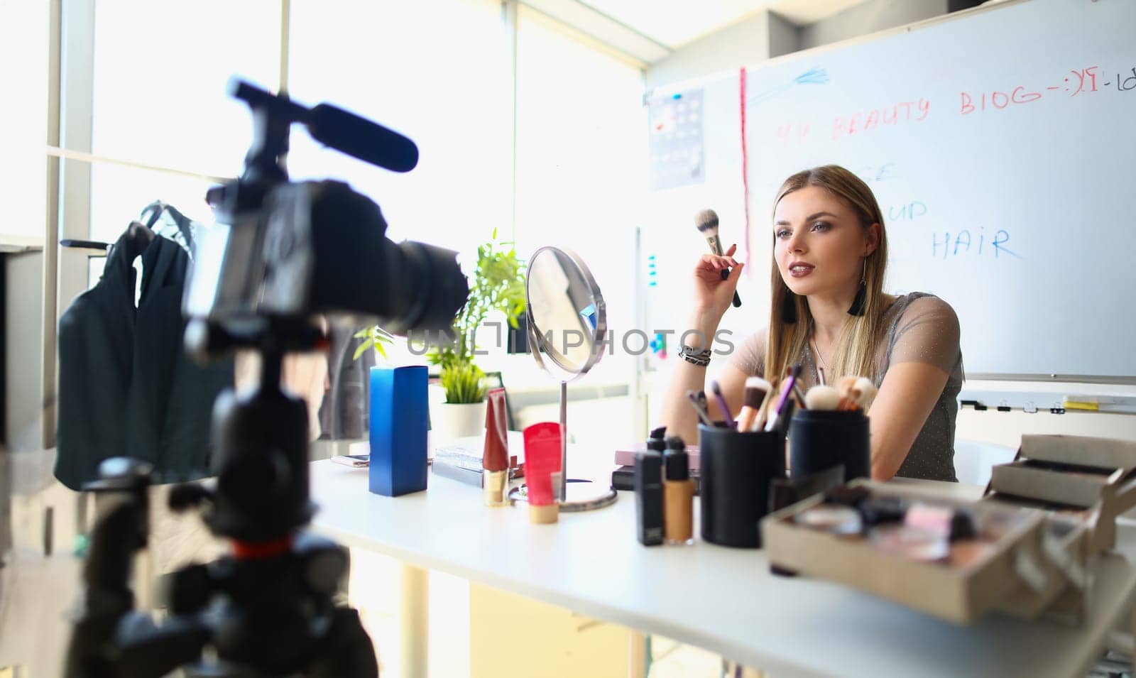 Woman talks about cosmetics with eye shadow blush palette and brushes recording online video. Woman blogger filming video for cosmetics blog
