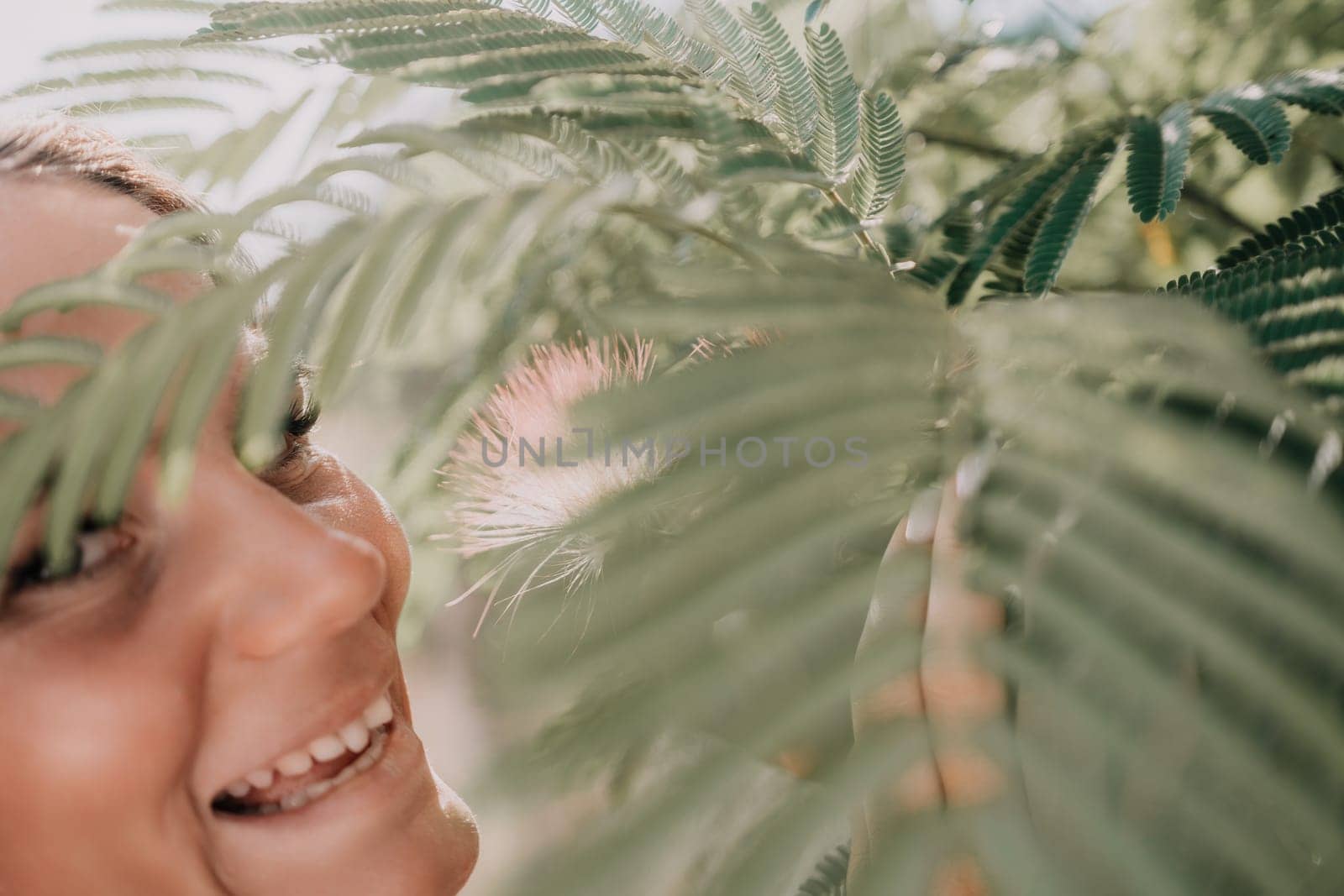Beauty portrait of happy woman closeup. Young girl smelling Chinese acacia pink blossoming flowers. Portrait of young woman in blooming spring, summer garden. Romantic vibe. Female and nature by panophotograph