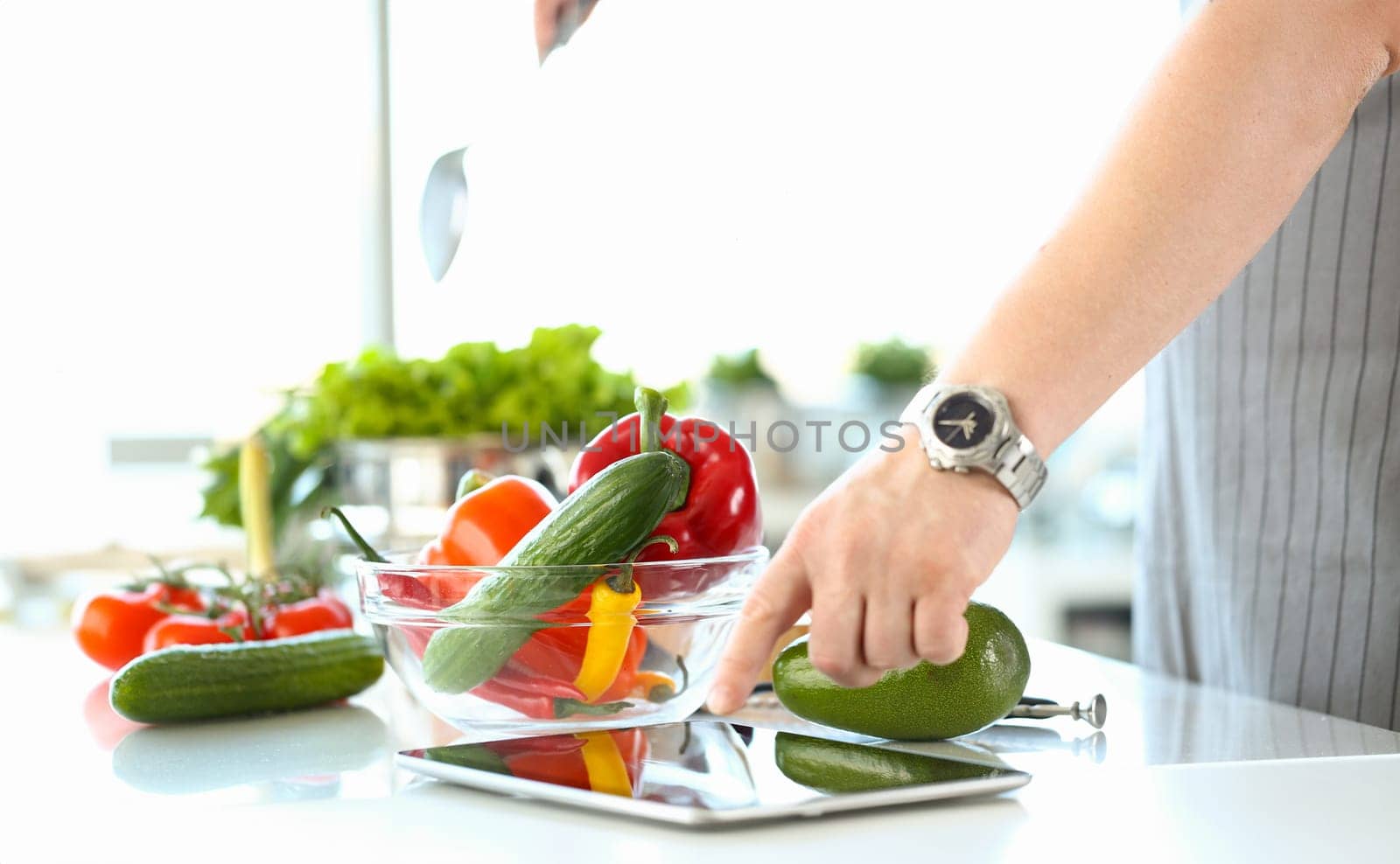 Chef following recipe on digital tablet preparing vegetable salad in kitchen. Online cooking course and recipe app
