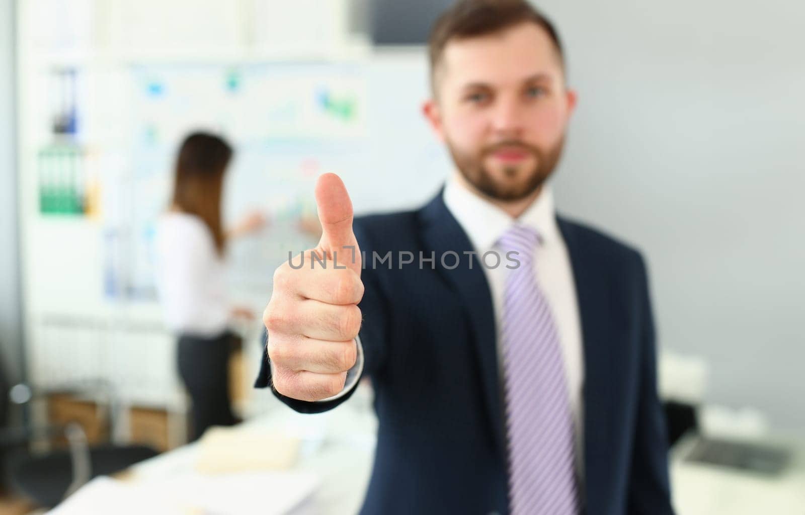 Businessman showing thumb up sign of success over blurred team of business people by kuprevich