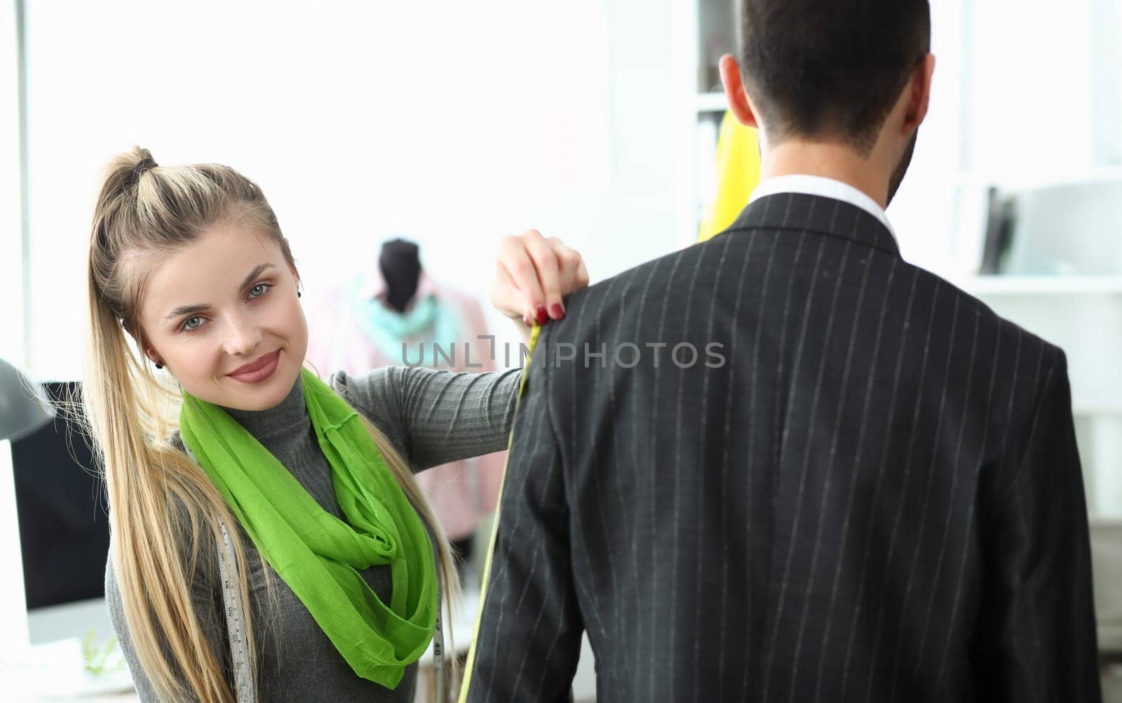 Young beautiful woman seamstress taking suit measurements from modern businessman in atelier by kuprevich