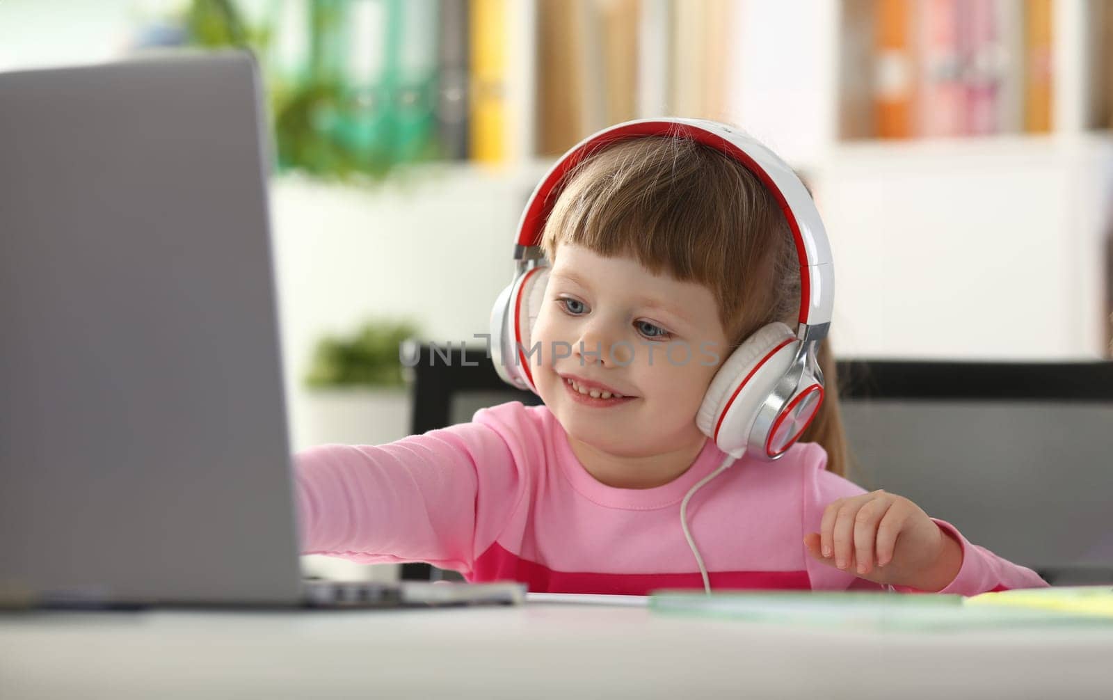 Portrait of a little child girl in headphones with laptop. Watching cartoons and kids remote learning concept