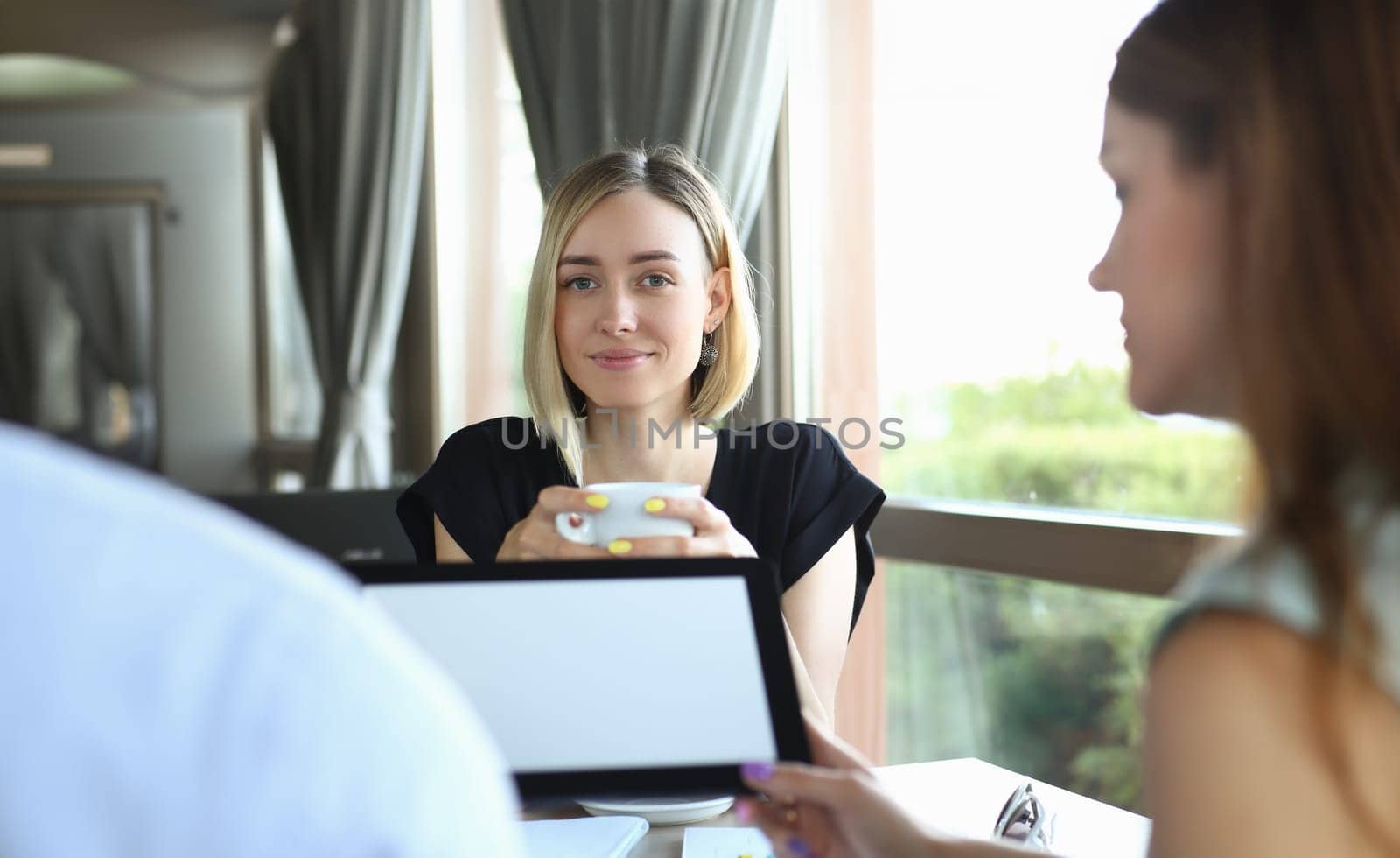 Group of young people at business meeting in cafe. Business people hold tablet at a meeting in cafe and discuss project