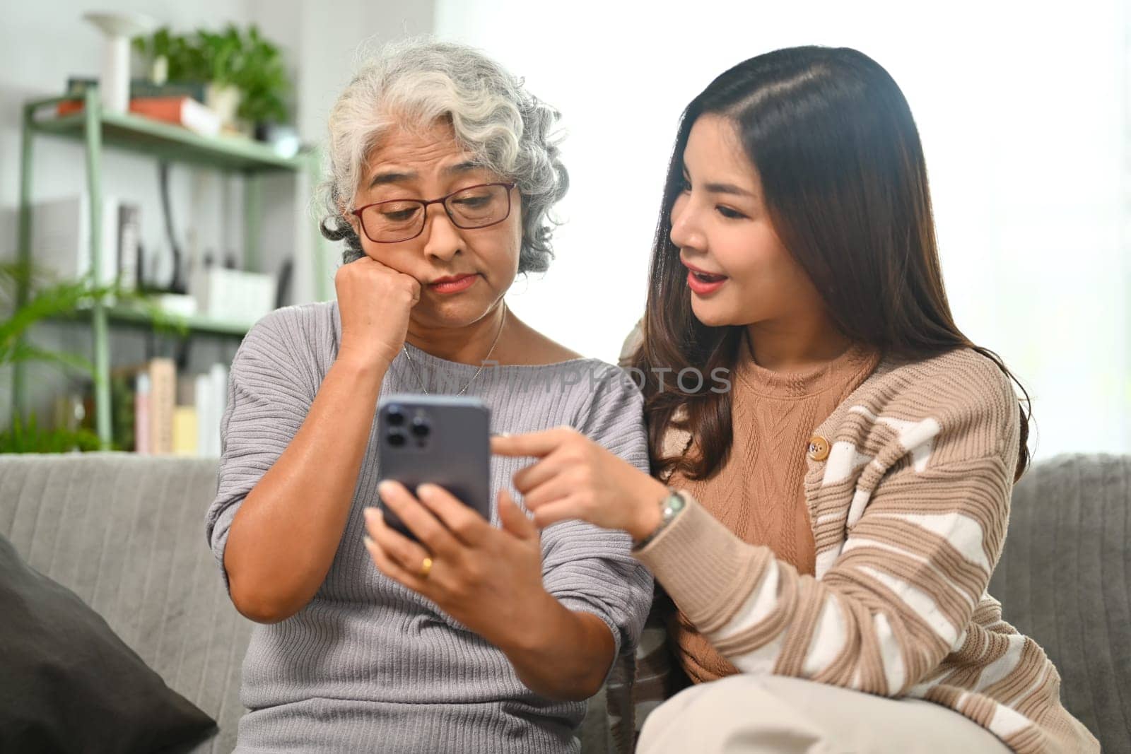 Young woman teaching mature mother using social networks on mobile phone. Elderly and technology concept.
