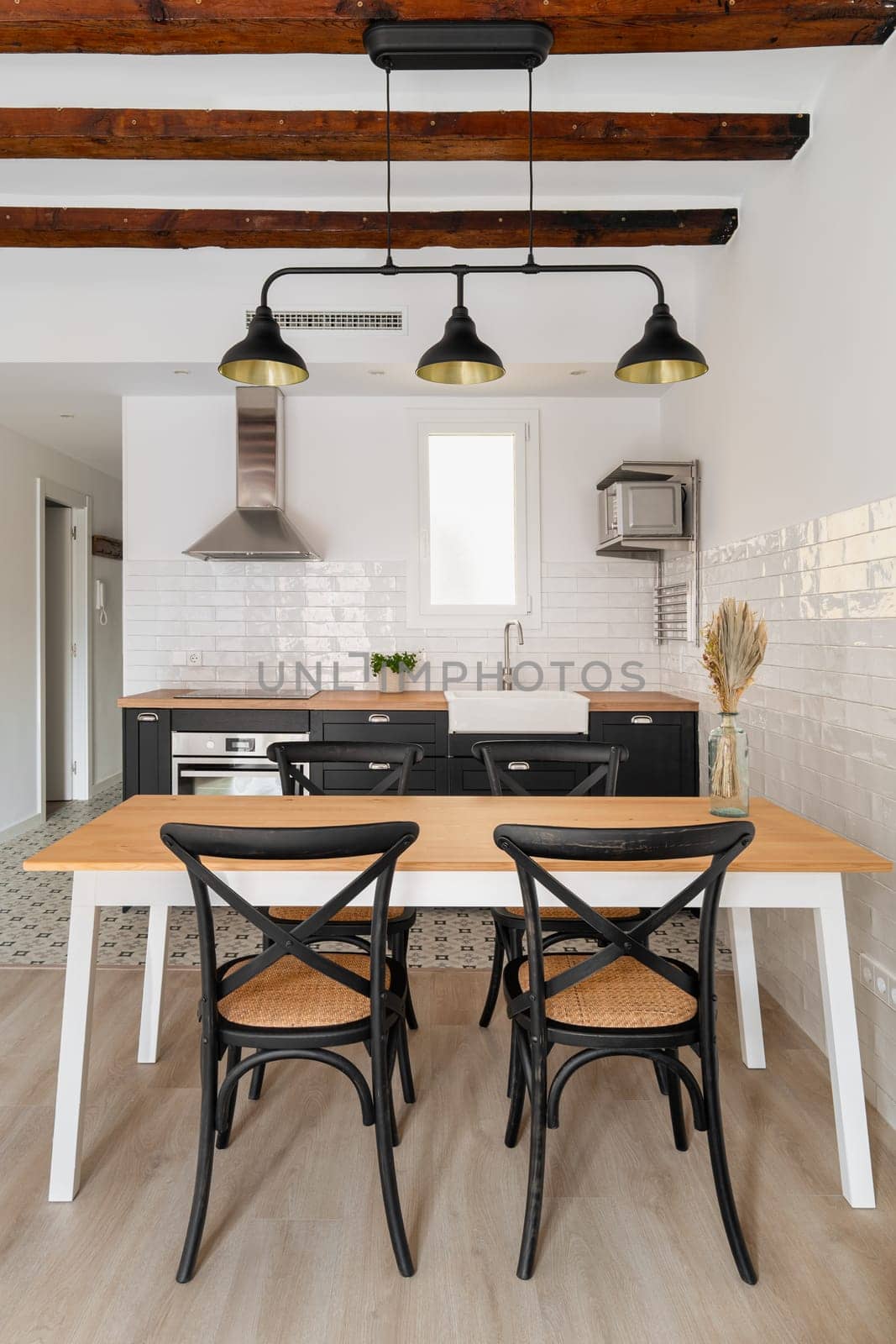 Dining table under vintage chandelier in studio apartment kitchen zone. Comfortable interior of minimalist cooking area in residential house