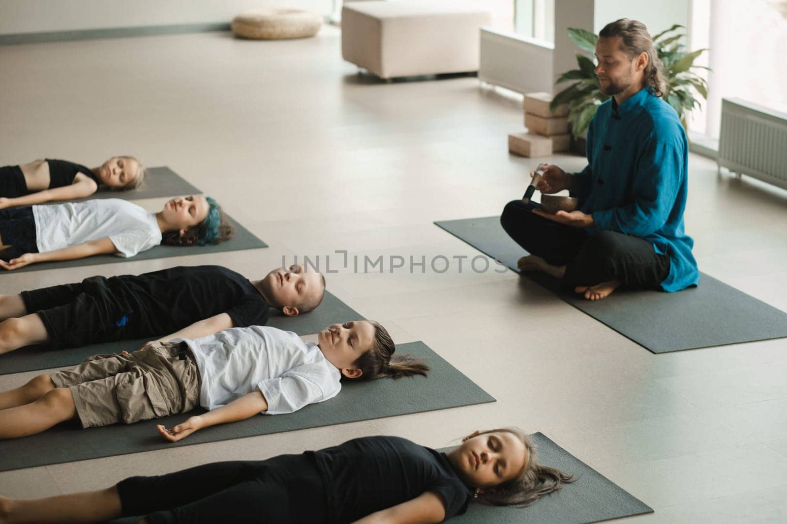Children relax lying down to the sounds of a Tibetan bowl in the fitness room. Children's yoga by Lobachad