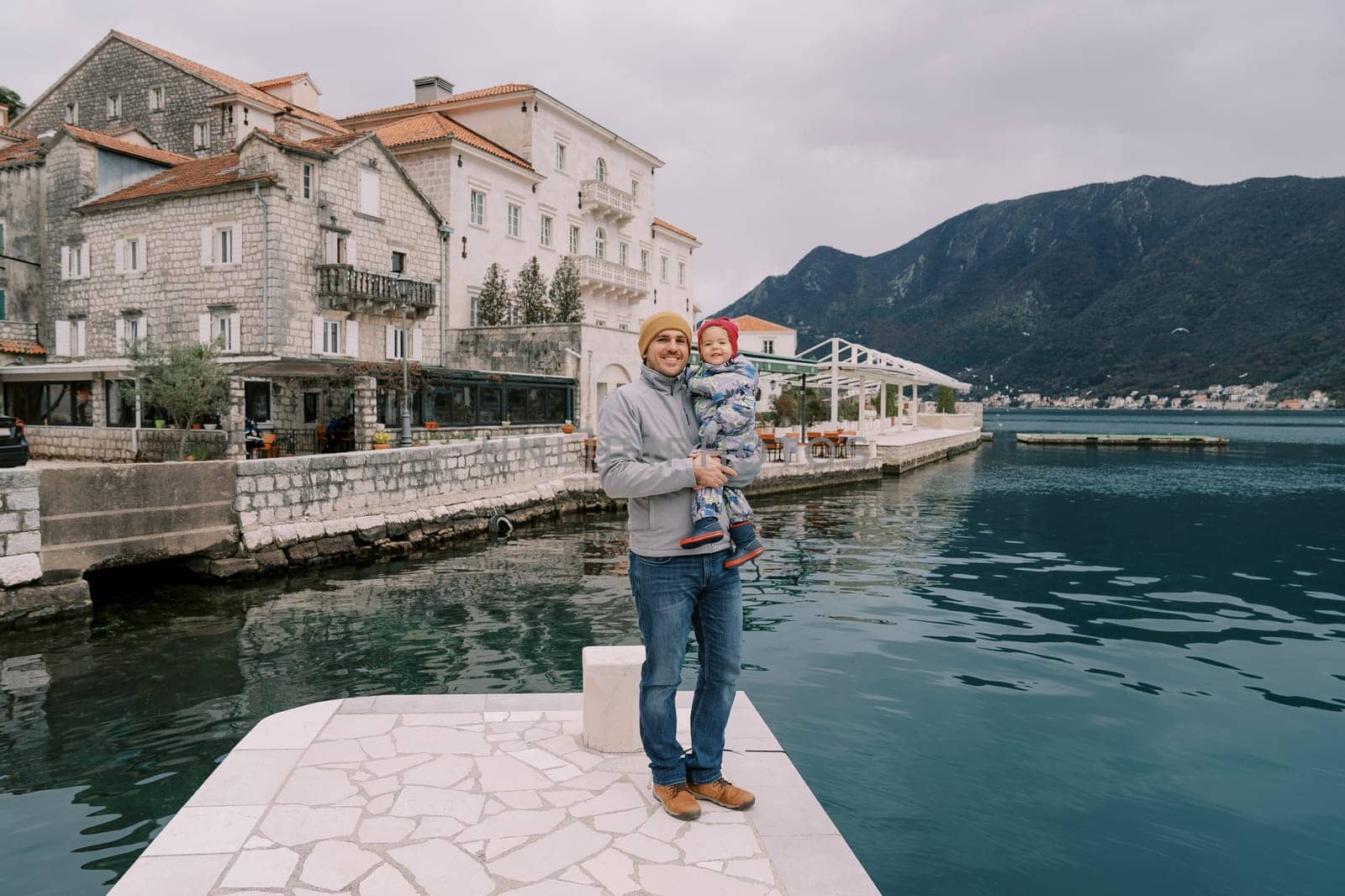 Dad with a little girl in his arms stands on the pier of the town of Perast. Montenegro. High quality photo