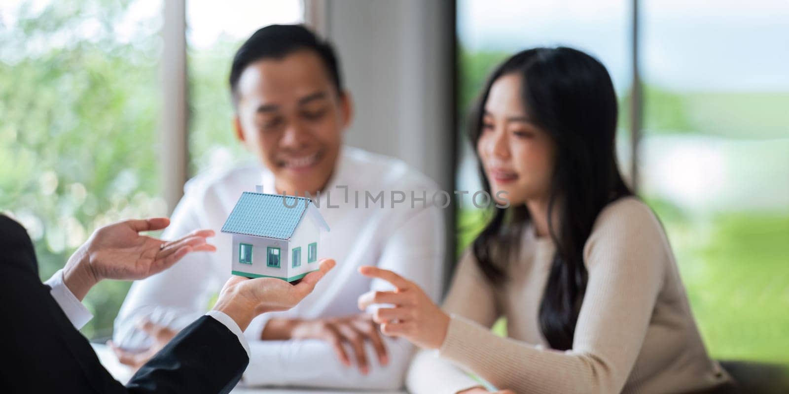 Young Asian couple making contract with house sale agency. man and his wife sitting signing the contract next to him looking the contract document with smile. real estate agreement successful concept.