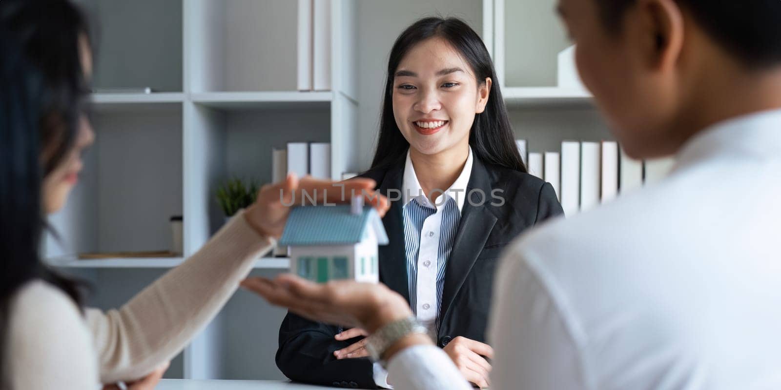 Young Asian couple making contract with house sale agency. man and his wife sitting signing the contract next to him looking the contract document with smile. real estate agreement successful concept.