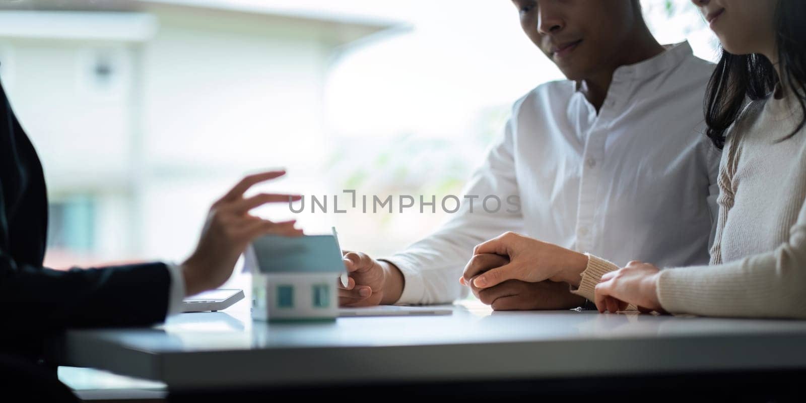 Young Asian couple making contract with house sale agency. man and his wife sitting signing the contract next to him looking the contract document with smile. real estate agreement successful concept.