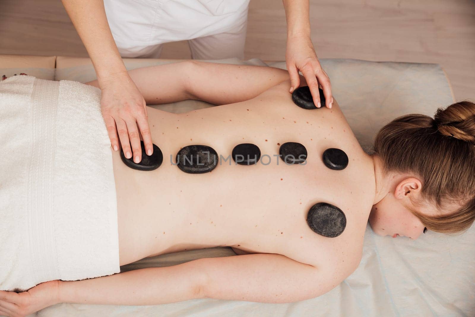 The masseur gives a back massage with stones to the client in the Health room