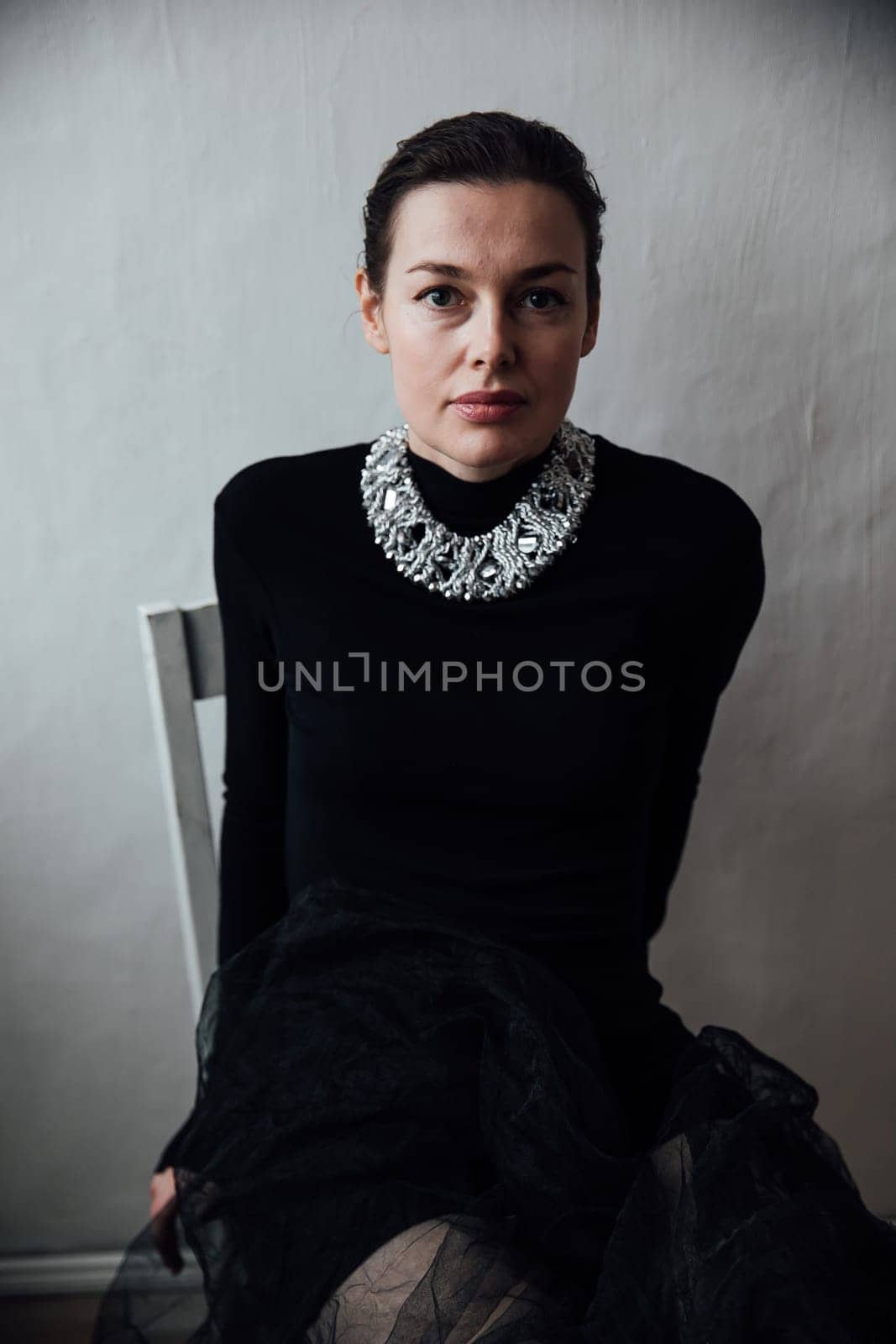 woman in black dress on white background sitting on a chair