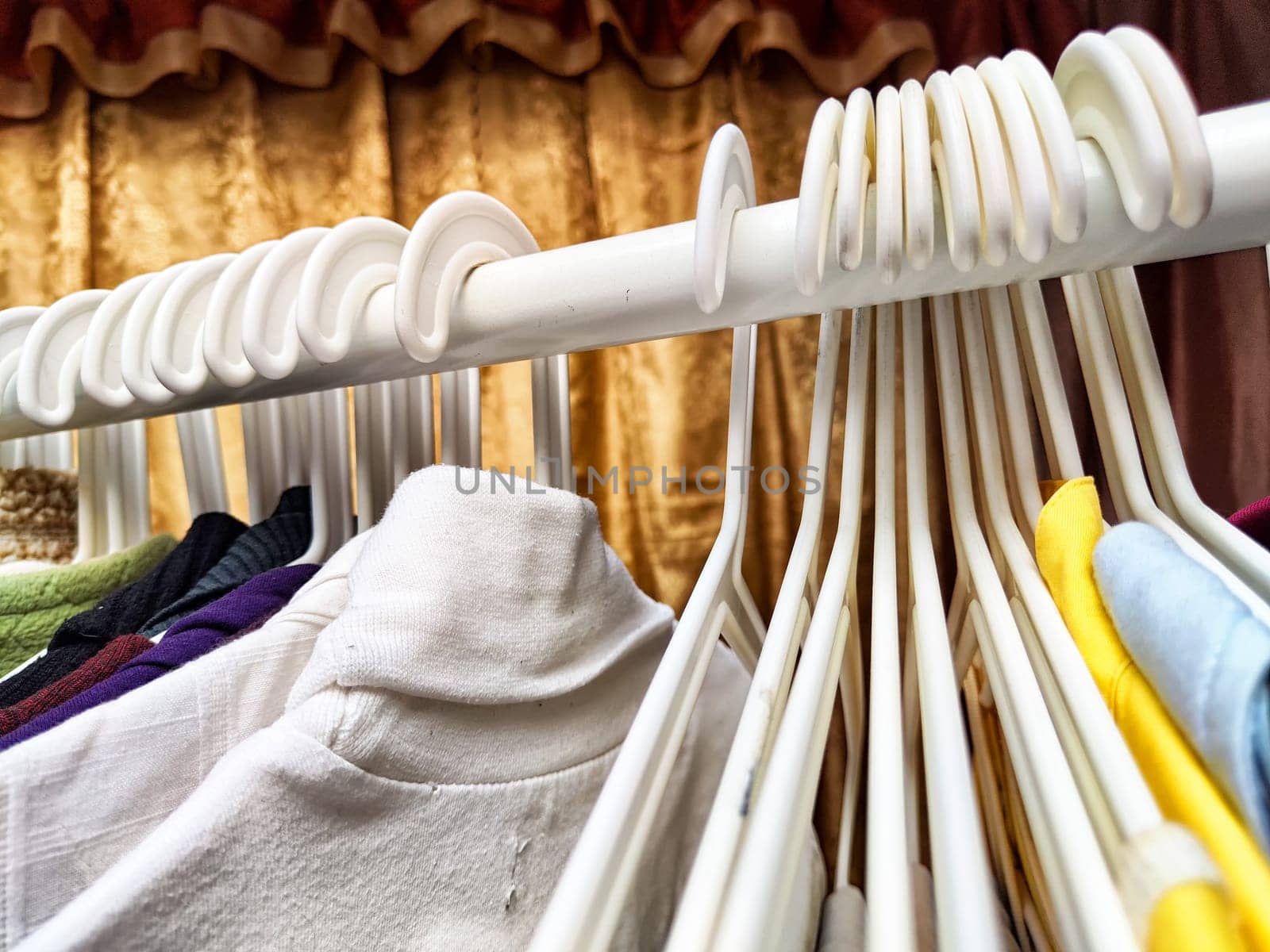 Hangers with a variety of clothes on white rack. Home storage of clothes. Clutter. Littery. Declutter. Garage sale