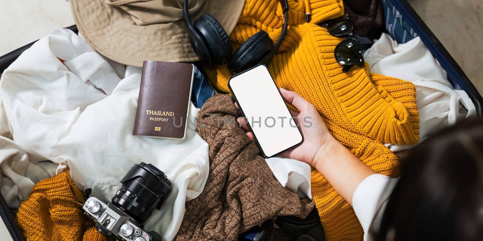 Woman using mobile phone blank white screen display frameless modern design while pack clothes a suitcase ready for travel by nateemee