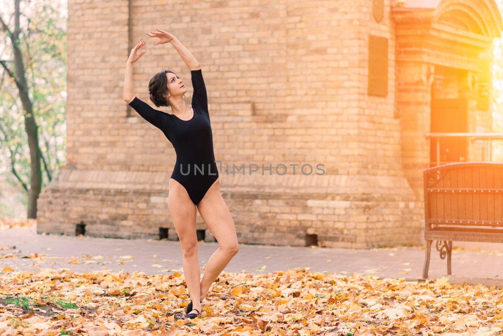 Beautiful female, ballerina, athlete in black bodysuit training in park