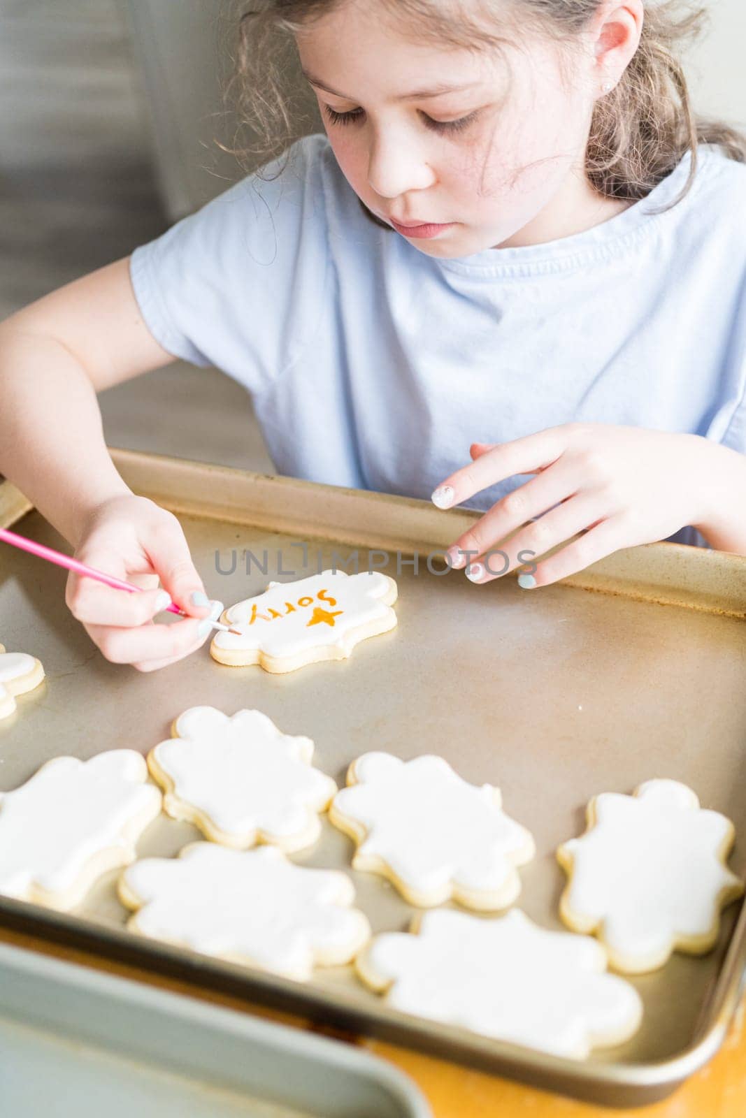 A heartwarming scene of a little girl carefully writing 'Sorry' on sugar cookies with food coloring, the cookies beautifully flooded with white royal icing.